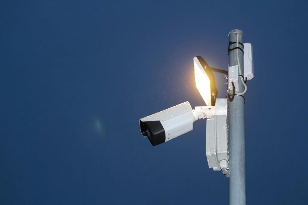Low angle view of a security camera and light against a dark blue night sky.